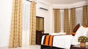 A hotel room with a bed, curtains, a nightstand, a mirror, and a potted plant. - Mamma Raji Hotel (Negombo)