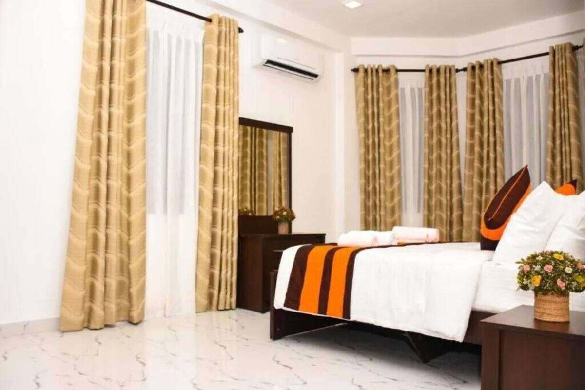 A hotel room with a bed, curtains, a nightstand, a mirror, and a potted plant.