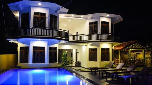 A two-story house with a swimming pool, a balcony, and a patio area with lounge chairs. - Mamma Raji Hotel (Negombo)