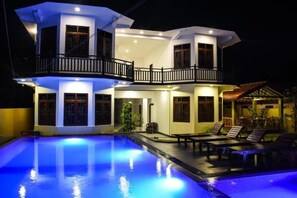 Una casa de dos pisos con piscina, balcón y zona de patio con sillones de descanso.