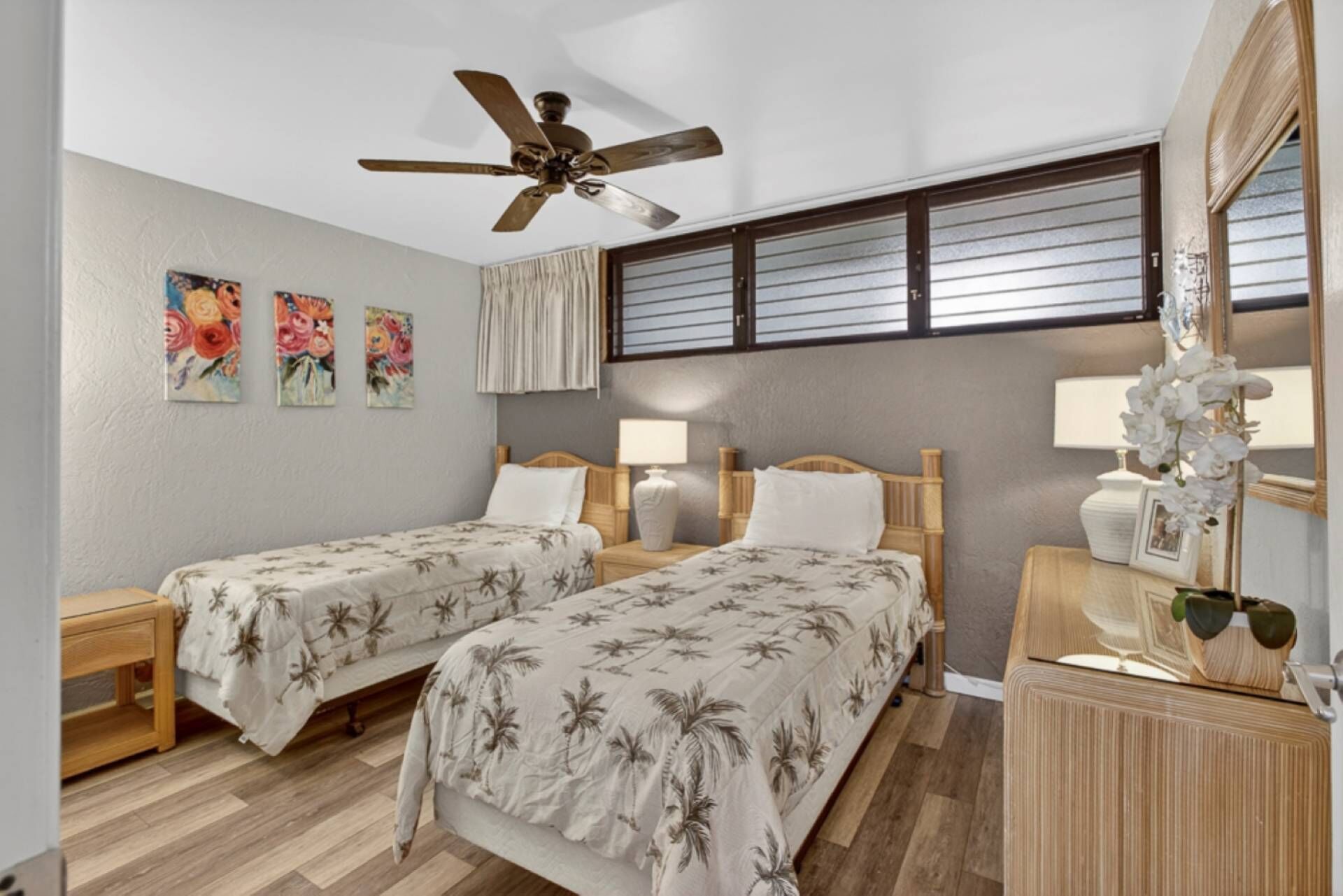 Ein Hotelzimmer mit zwei Einzelbetten, einem Deckenventilator, einem Fenster mit Jalousien und einem Spiegel mit Blumenvase.