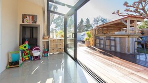A modern interior with a glass door leading to an outdoor deck, wooden flooring, and a children's play area with toys.