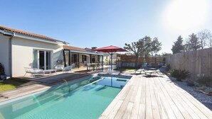 A wooden deck with a swimming pool, lounge chairs, and a red umbrella.
