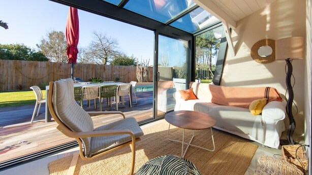 A modern living room with a glass wall, a sofa, a chair, and a small table.
