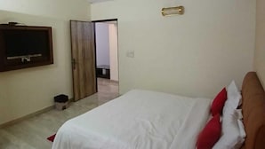 A bedroom with a bed, a ceiling fan, a television, and a door leading to another room. - Shree Krishna Valley (Vrindavan)