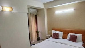 A hotel room with a bed, a ceiling fan, a red rug, and a nightstand. - Shree Krishna Valley (Vrindavan)