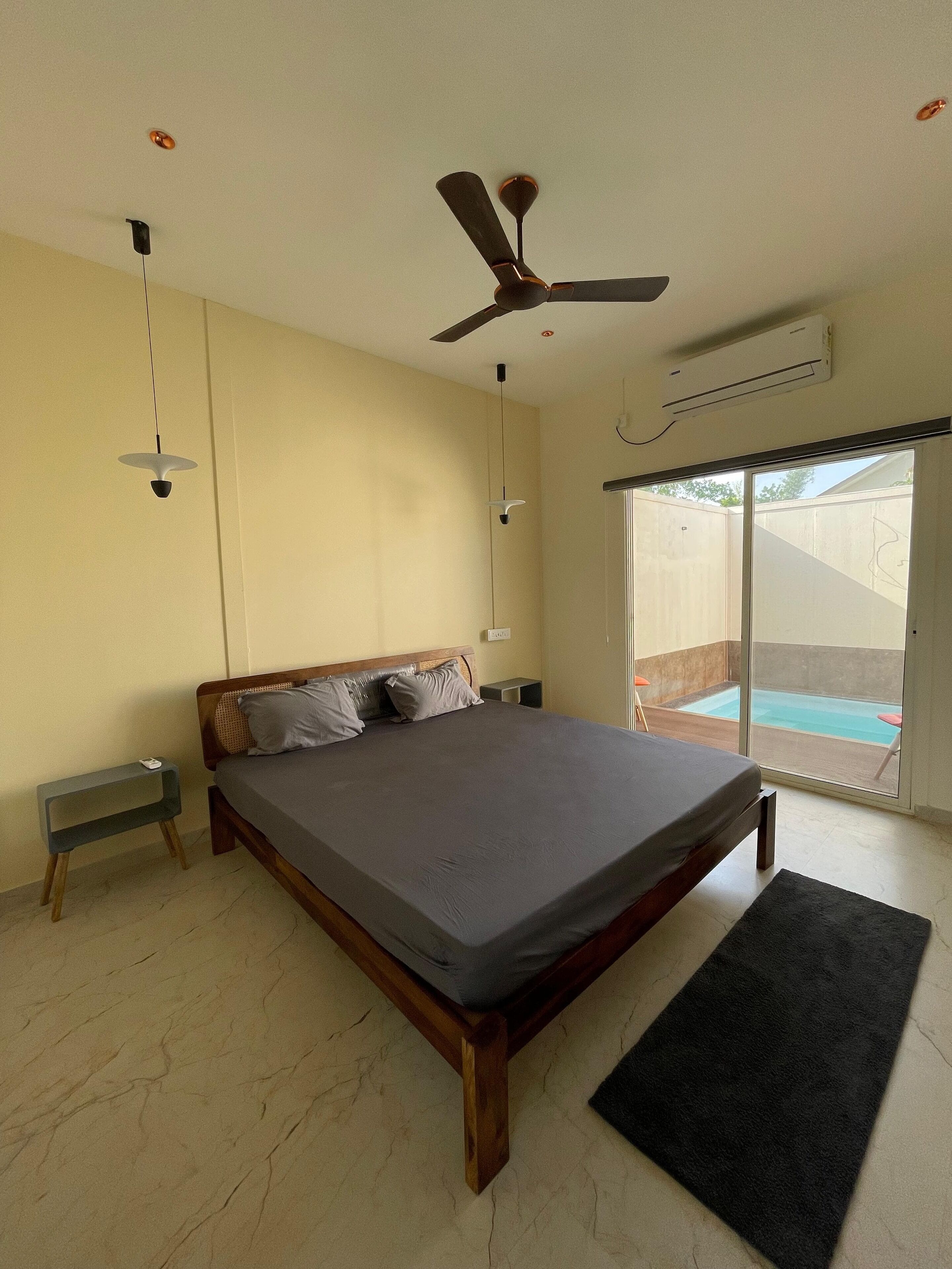 A bedroom with a large bed, a ceiling fan, a small table, and a view of a swimming pool.