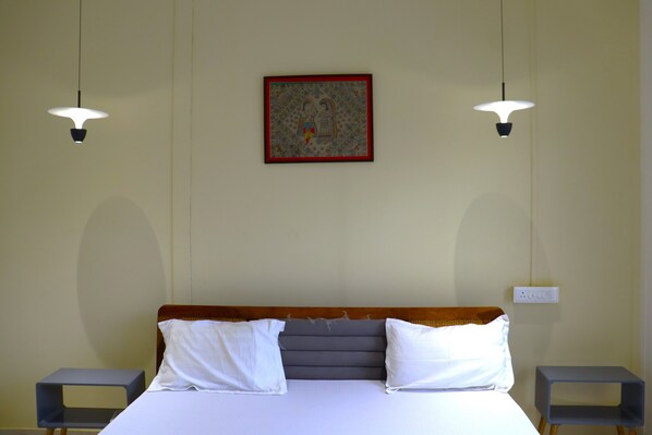 Habitación de hotel con una cama, dos mesitas de noche, una lámpara de pie y dos lámparas colgantes, además de un cuadro en la pared.