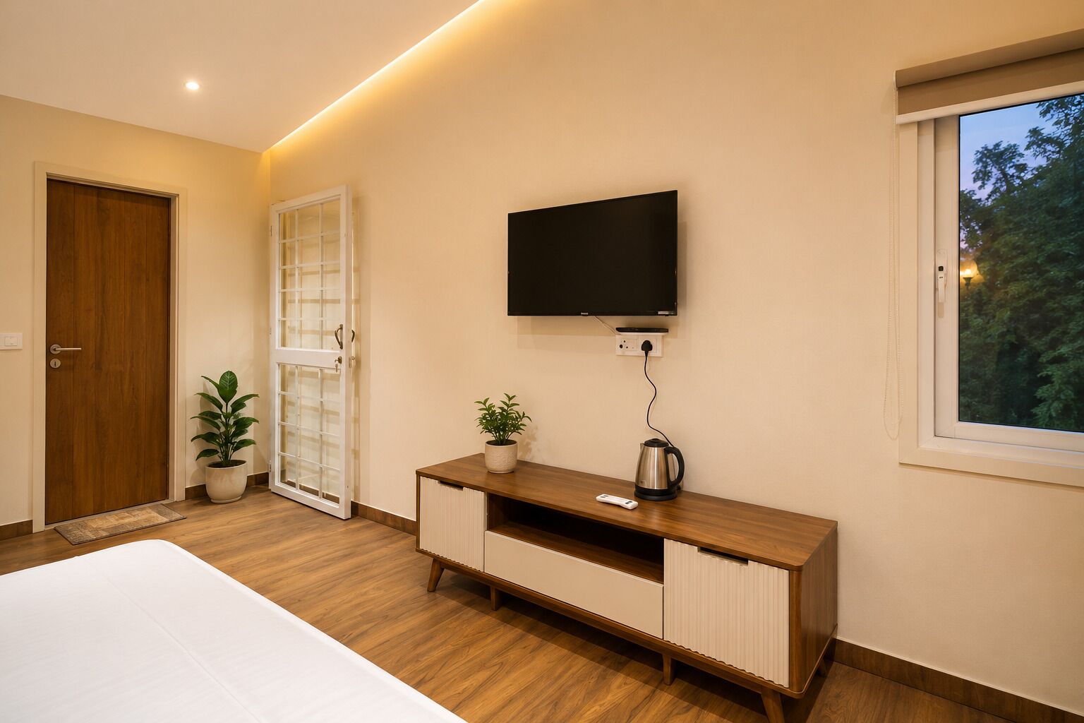 Una camera da letto con un letto, una TV a parete, un armadio in legno, una pianta in vaso e una finestra.