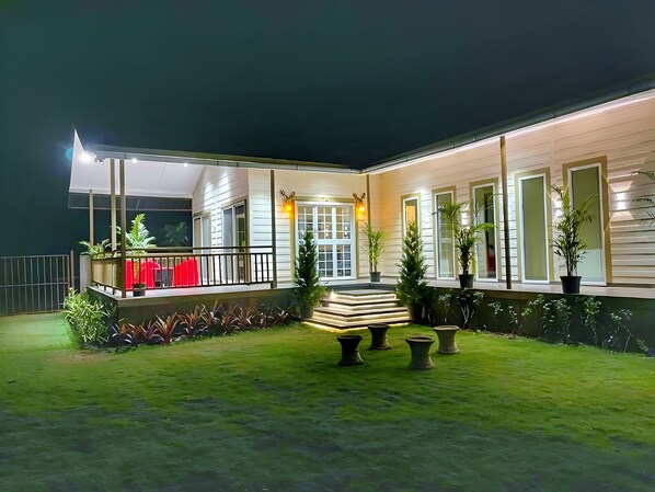 Un espacio exterior bien iluminado con zona de estar cubierta, plantas en macetas y una escalera que conduce a una entrada techada.