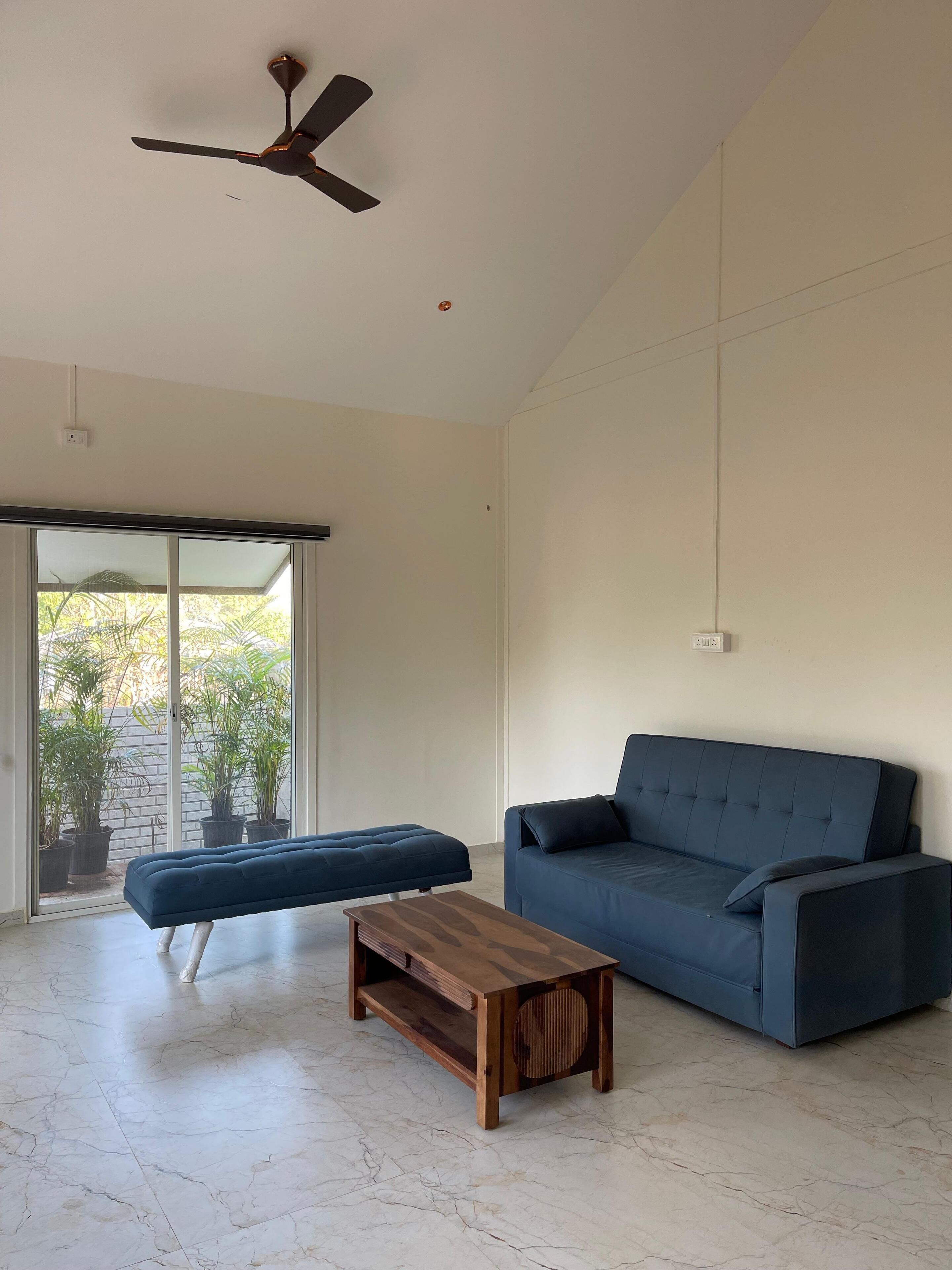 A spacious living room with a dark blue sofa, a wooden coffee table, and a ceiling fan.