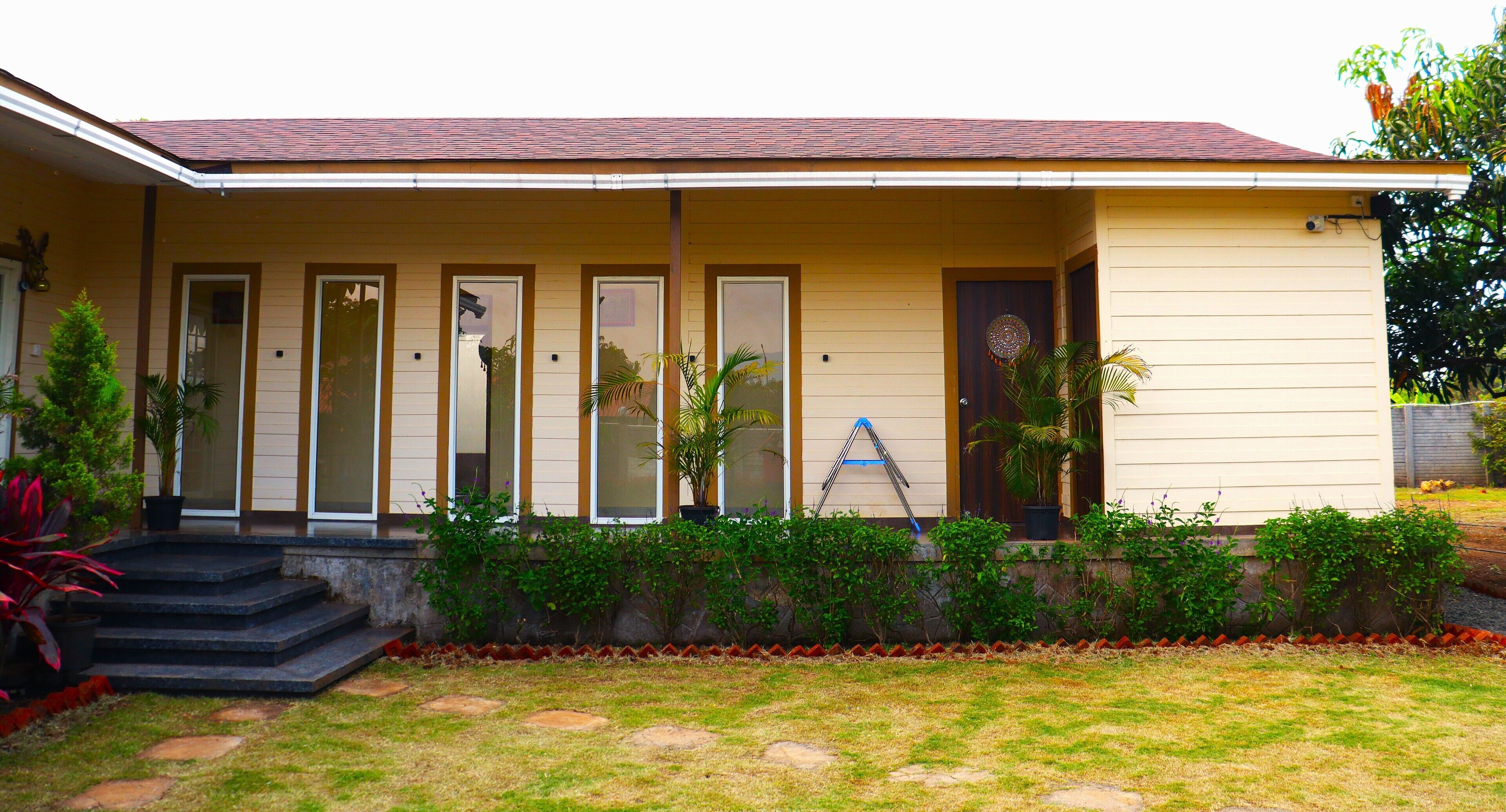 A two-story house with a covered porch, multiple windows, and a small garden area with stepping stones and potted plants.