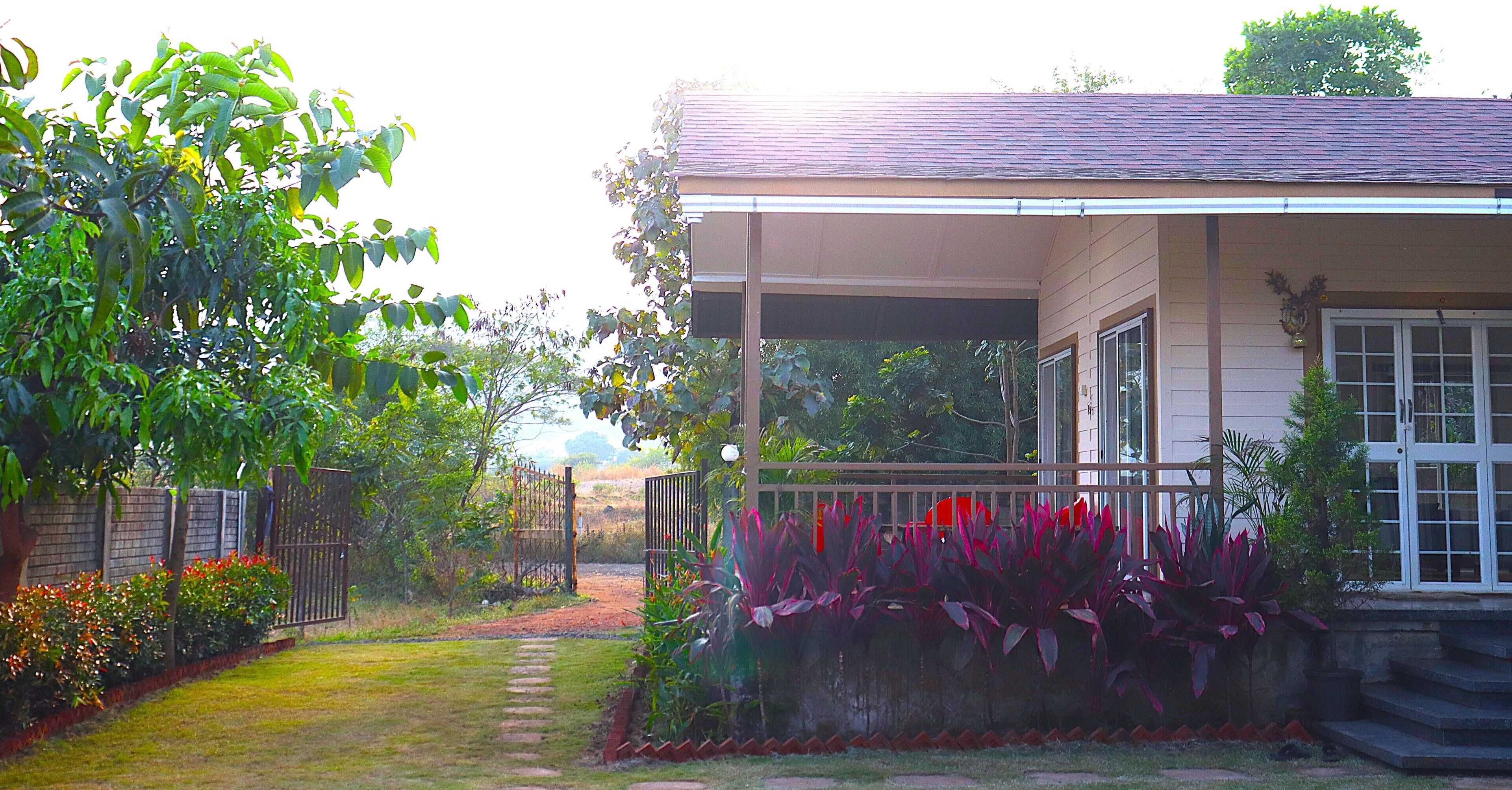A house with a covered porch, a garden with red flowers, and a brick wall.