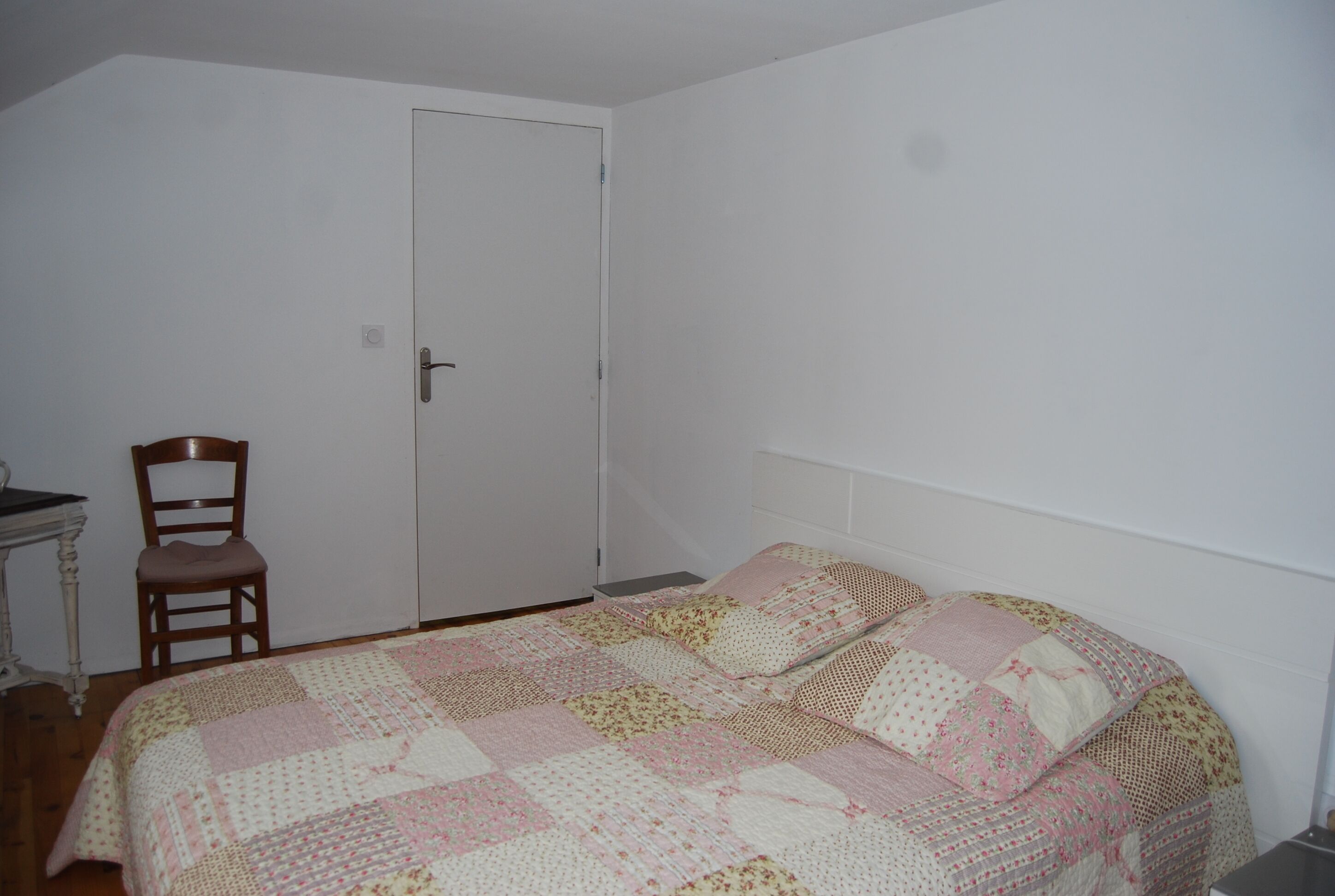 A bedroom with a bed, a chair, and a door.