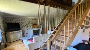 Una escalera de madera con un bolso colgando, un sofá blanco y un televisor en una habitación con paredes de estilo piedra.