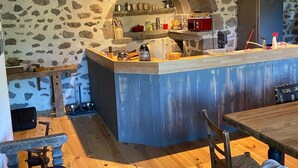 Una cocina rústica con pared de piedra, vigas de madera y una isla central con pileta y estufa.