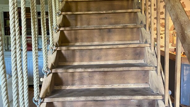 Una escalera de madera con barandilla y balaustres de cuerda.