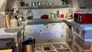 Una cocina con paredes de piedra, horno empotrado, suelo de madera y diversos utensilios y electrodomésticos.