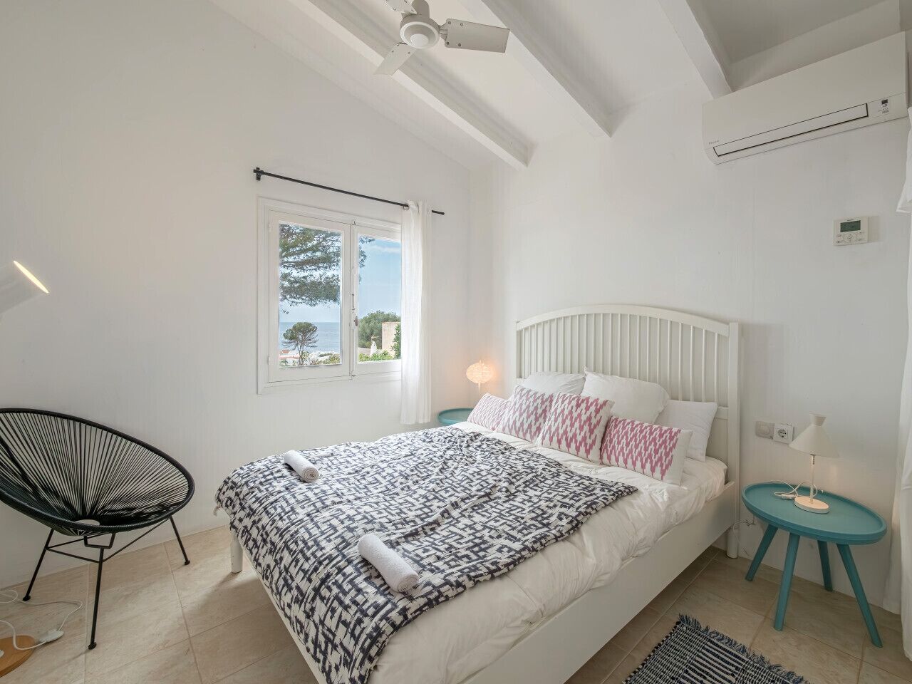 A bedroom with a bed, a chair, a nightstand, and a window.