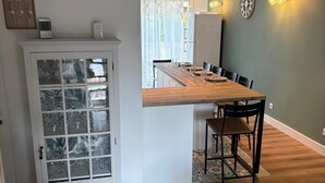 A dining area with a wooden table and chairs, a white cabinet with glass doors, and a green wall with wall clocks.