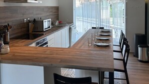 A modern kitchen with a wooden island, white cabinets, and a large window with sheer curtains.