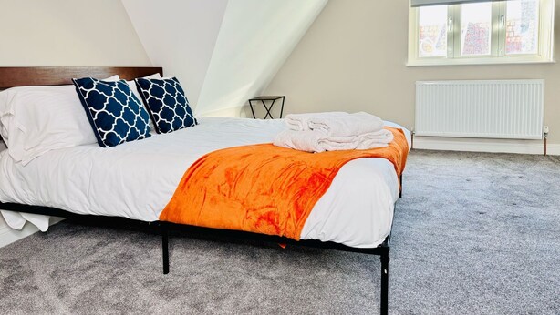 A bedroom with a bed, pillows, a blanket, a radiator, and a window. - 25A Moonstone House in Thetford (Thetford)