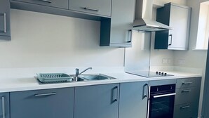 Et moderne køkken med lysegrå skabe, en stålvask og en ovn.