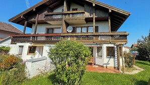 Ein zweistöckiges Holzhaus mit Balkon, umgeben von viel Grün.