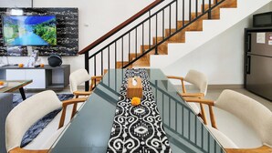 A modern living room with a staircase, a dining area with a patterned runner, and a television mounted on the wall.