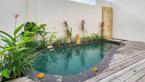 A swimming pool with a wooden deck, surrounded by various plants and a statue.