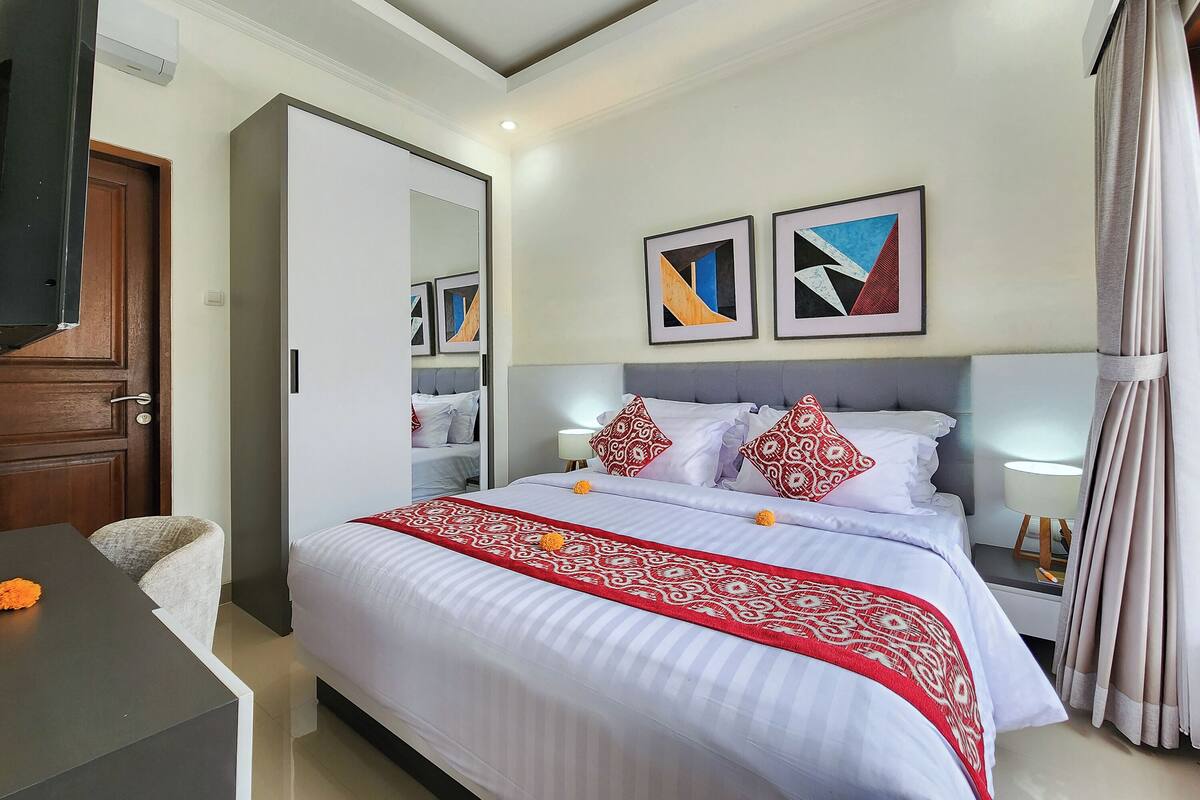 A hotel room with a bed, bedside tables, a wardrobe, and artwork on the wall.