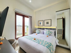 A hotel room with a bed, a desk, a chair, a TV, a balcony, and two framed pictures on the wall. - Villa Elemi Seminyak  by Nagisa Bali (Seminyak)