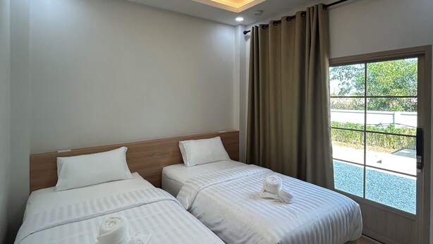 Een hotelkamer met twee bedden, een plafondlamp, een raam met gordijnen en uitzicht op groen.