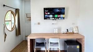 Een moderne kamer met een houten bureau, twee stoelen, een aan de muur bevestigde televisie en een kleine koelkast.
