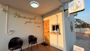Een receptiegedeelte met een houten vloer, twee zwarte stoelen, een muur met het opschrift 'Harmonized your escape', een houten deur en een bord met de tekst Zen Harmony House.