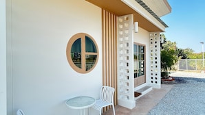 Een modern gebouw met een overdekte patio, compleet met twee witte metalen stoelen en een kleine ronde tafel.
