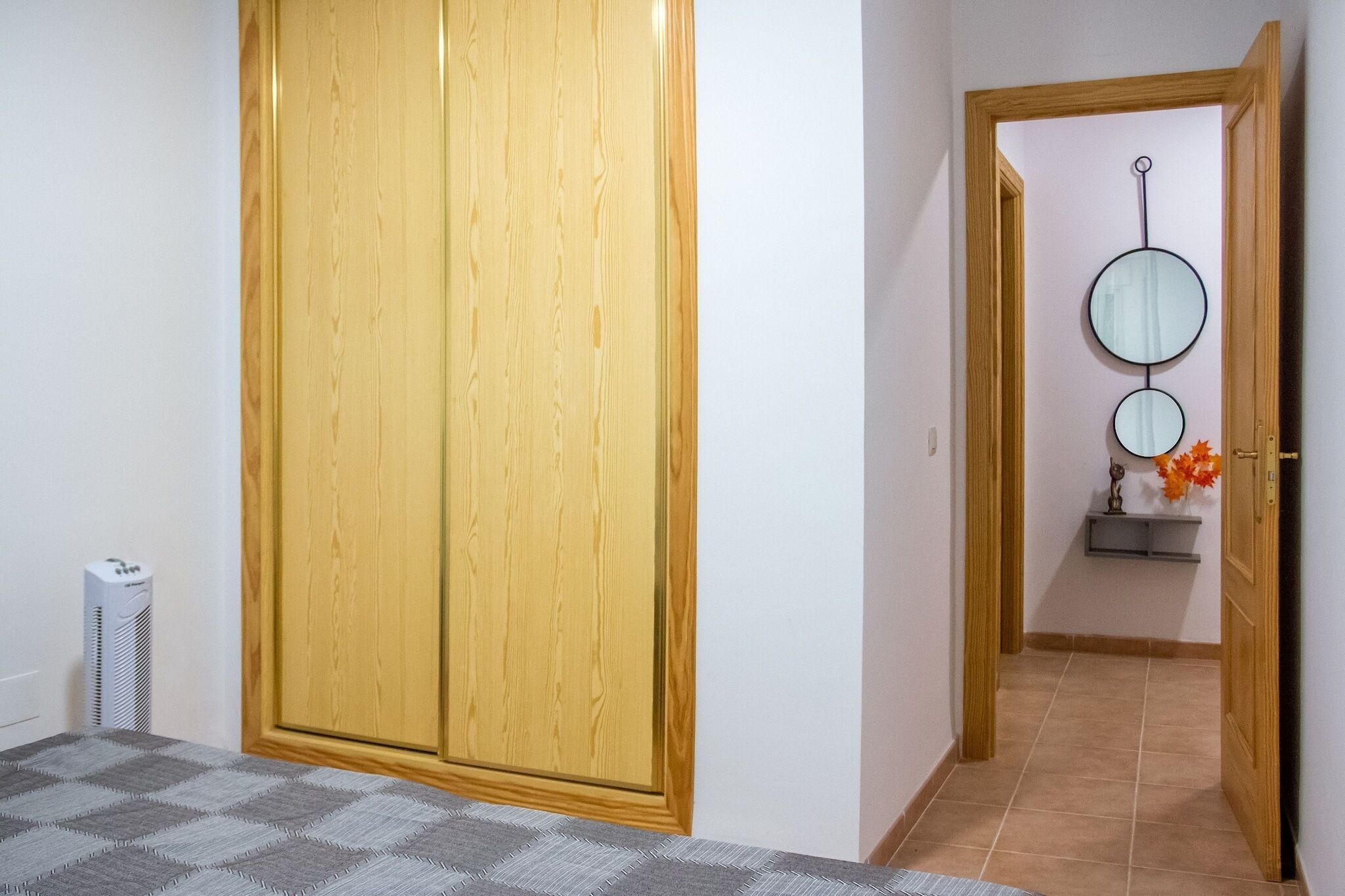 Un pasillo con un armario de madera, un espejo y un pequeño estante con flores.