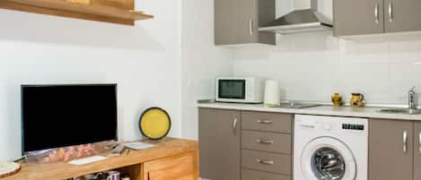 A compact kitchen with a washing machine, a microwave, and a wooden cabinet with a flat-screen TV.