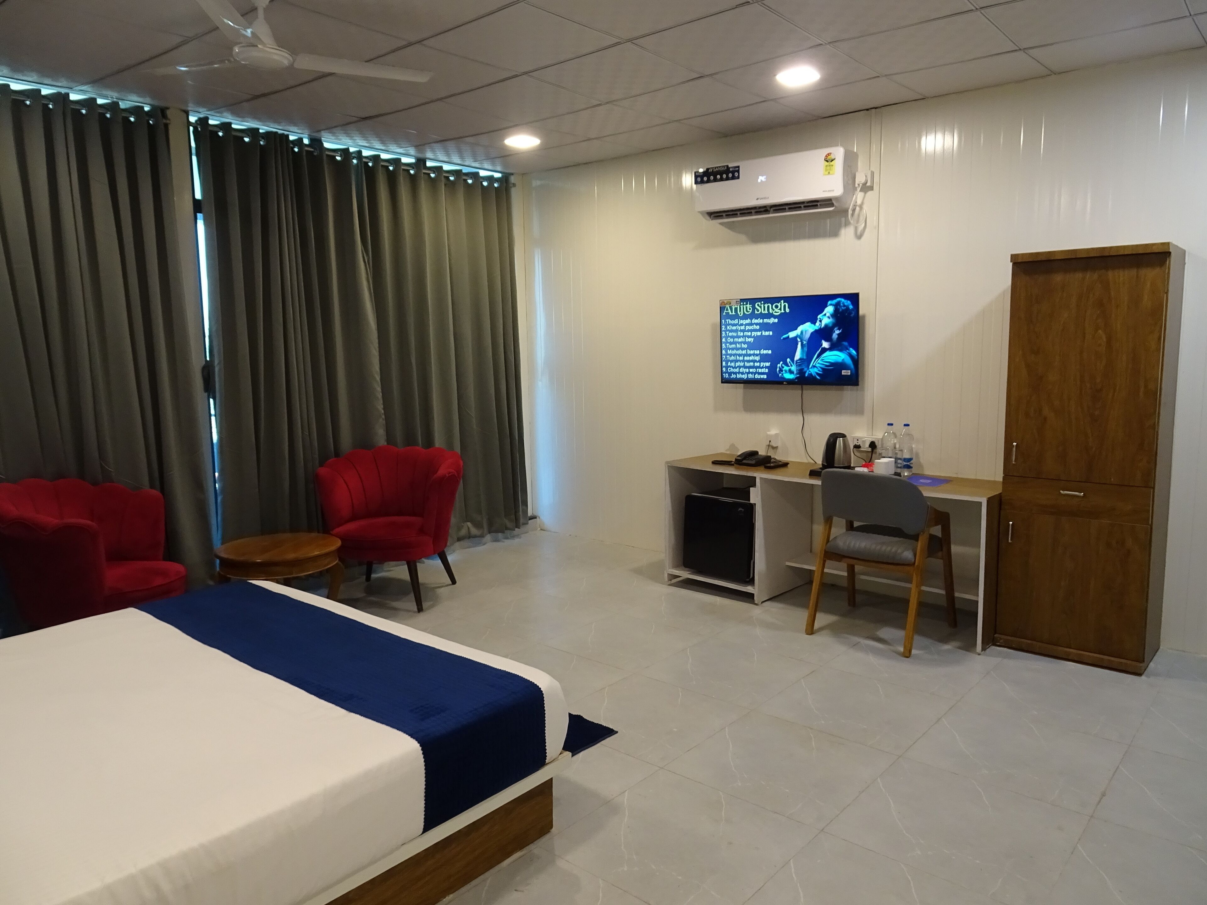 Una habitación de hotel con cama, escritorio, silla, televisor y armario.
