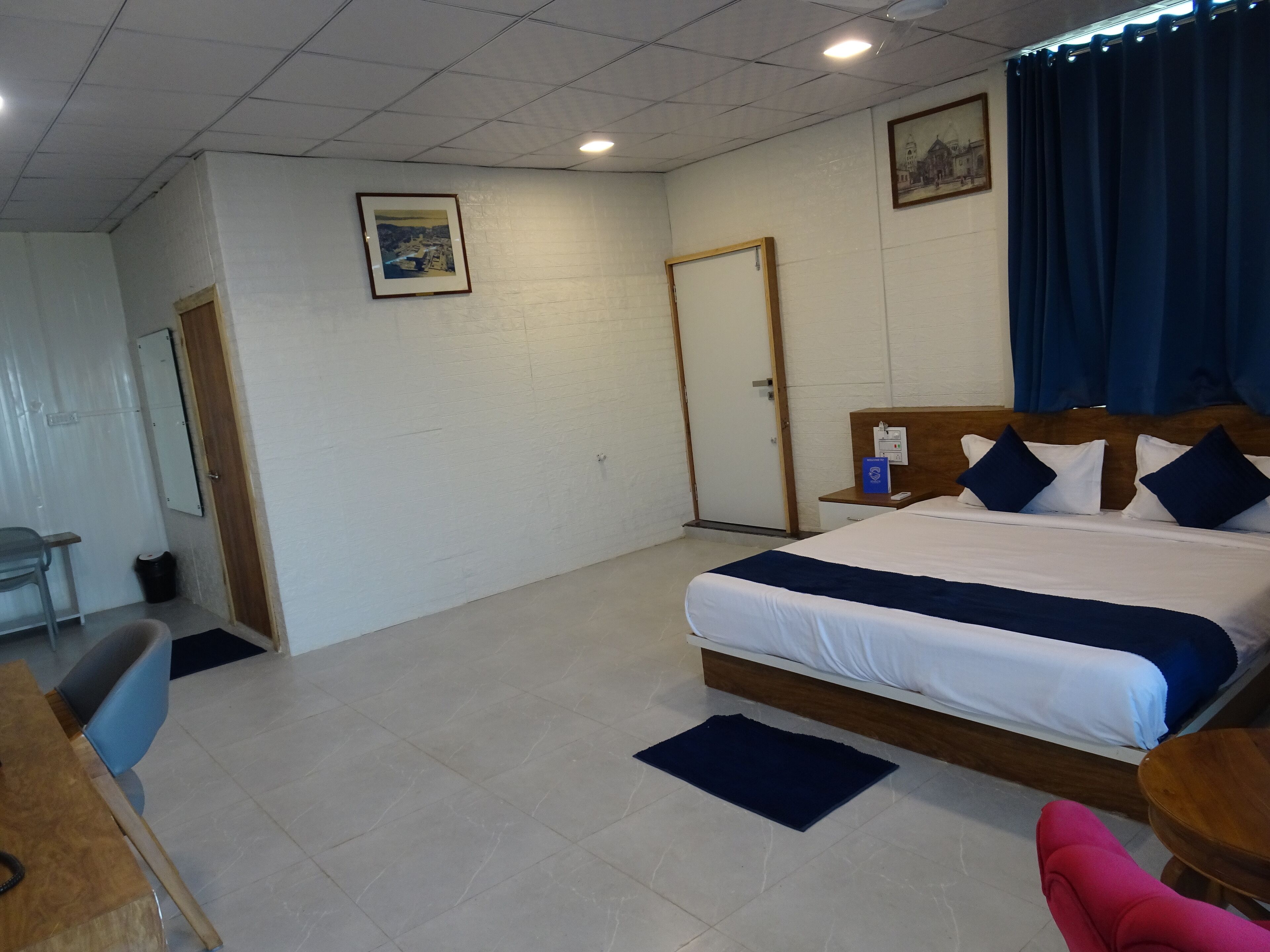 Una camera d'albergo con un letto, una scrivania, una sedia, un tavolino, una porta e un quadro appeso al muro.