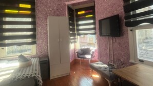 Ένα δωμάτιο με ένα κρεβάτι, ένα γραφείο, μια καρέκλα, μια ντουλάπα και μια τηλεόραση.