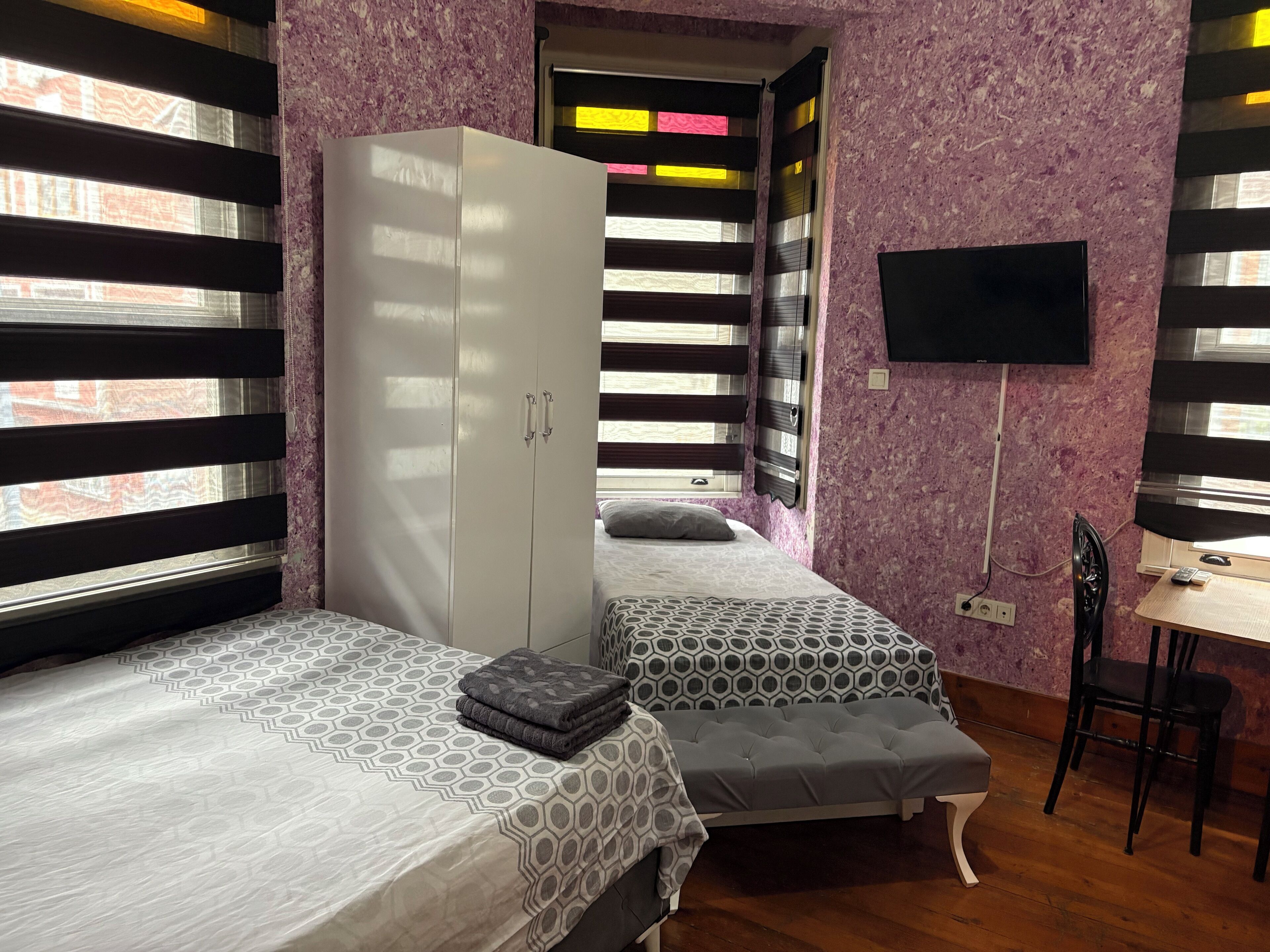 A bedroom with two beds, a wardrobe, a desk, and a TV.