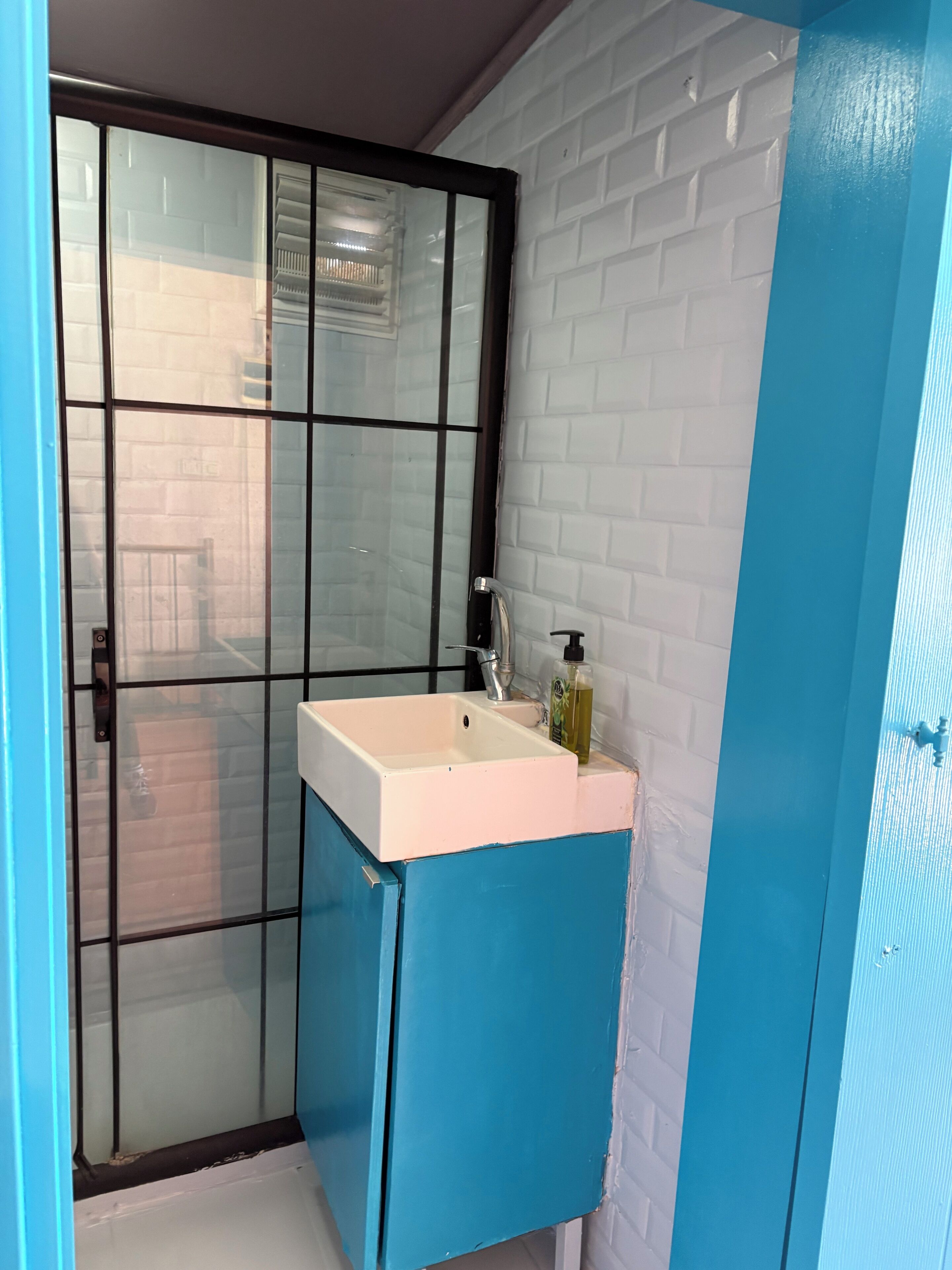 A bathroom with a white sink, a blue cabinet, and a glass door.