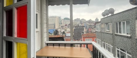 Ein Balkon mit Tisch und Stühlen, Blick auf die Stadtlandschaft und eine Tür mit farbenfrohen Paneelen.