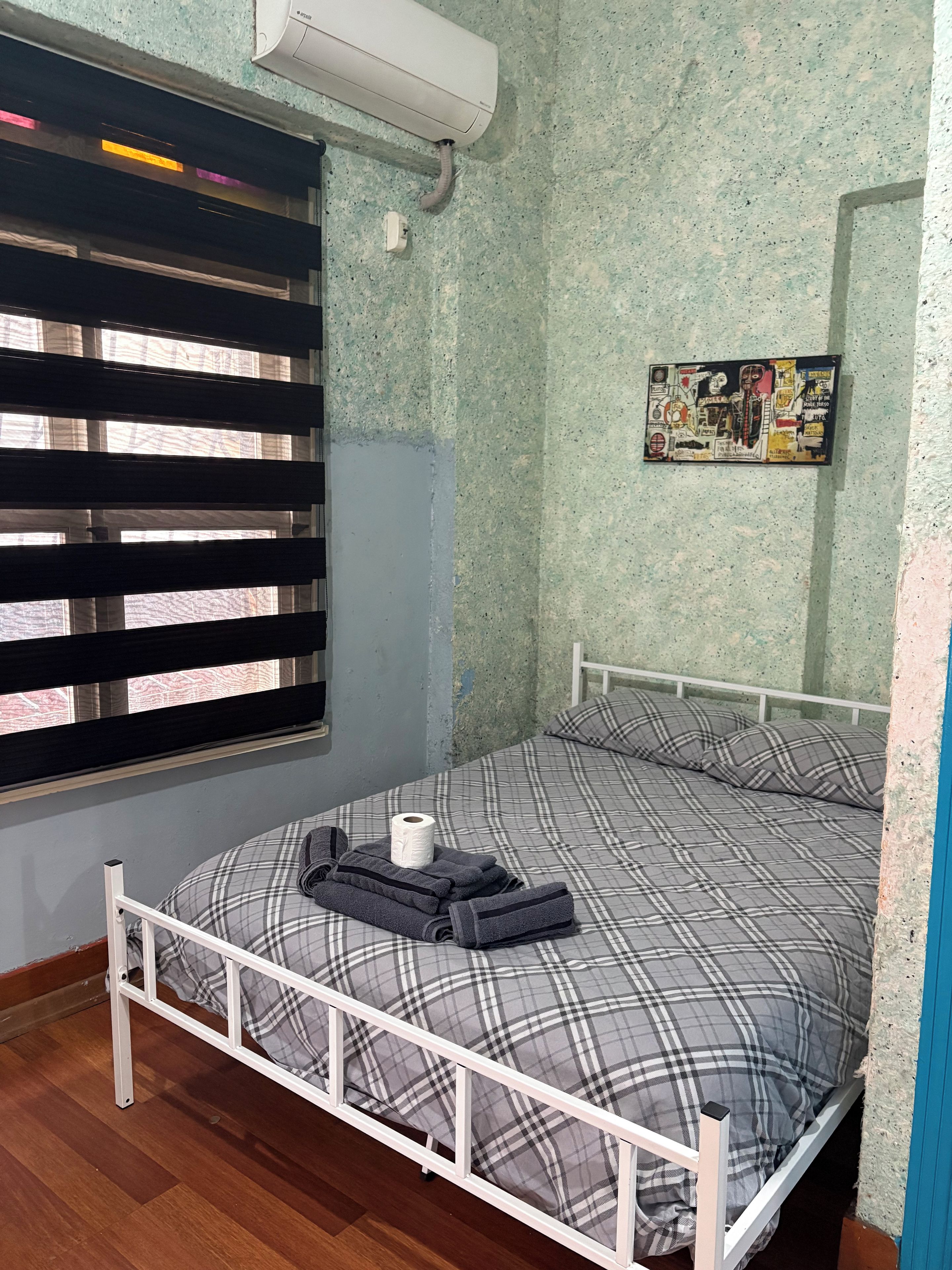 A room with a bed, a window with blinds, an air conditioning unit, and a wall with a poster.