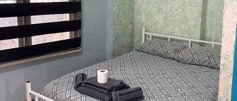 A room with a bed, a window with blinds, an air conditioning unit, and a wall with a poster.
