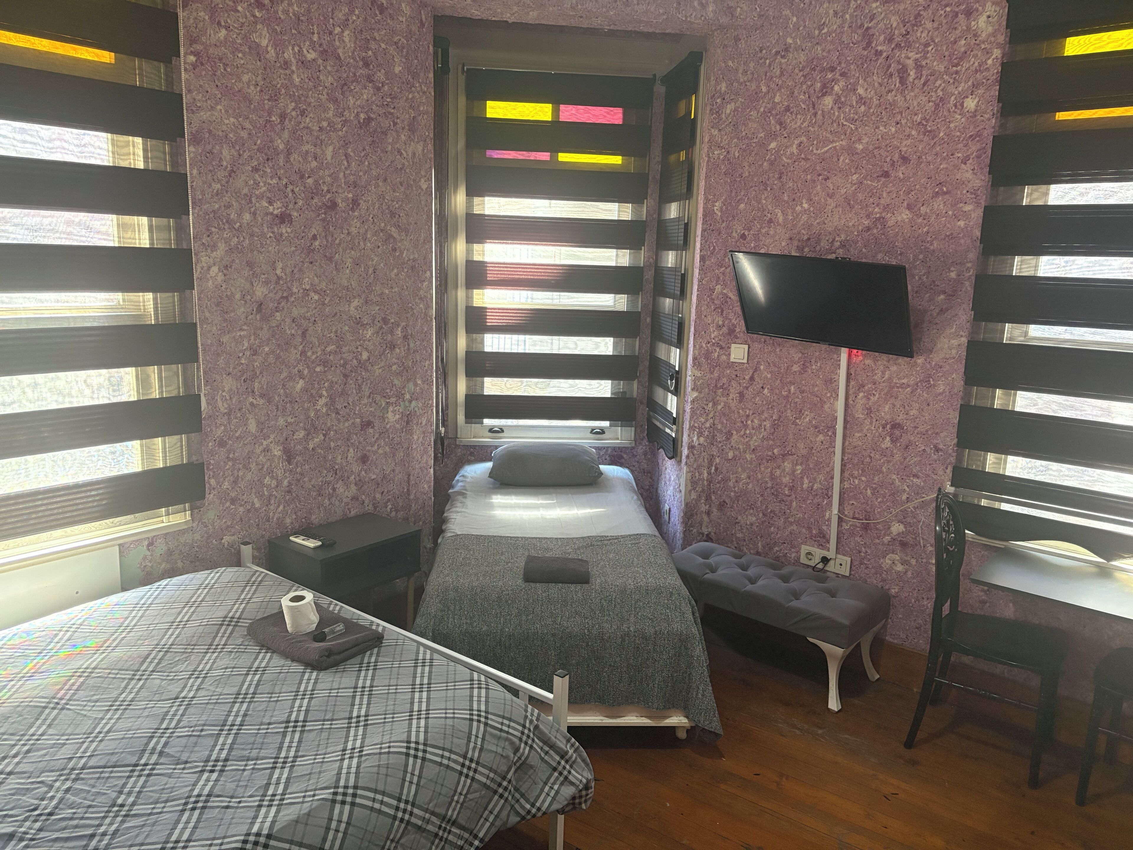 A room with a bed, a bench, a TV, and a window with blinds.