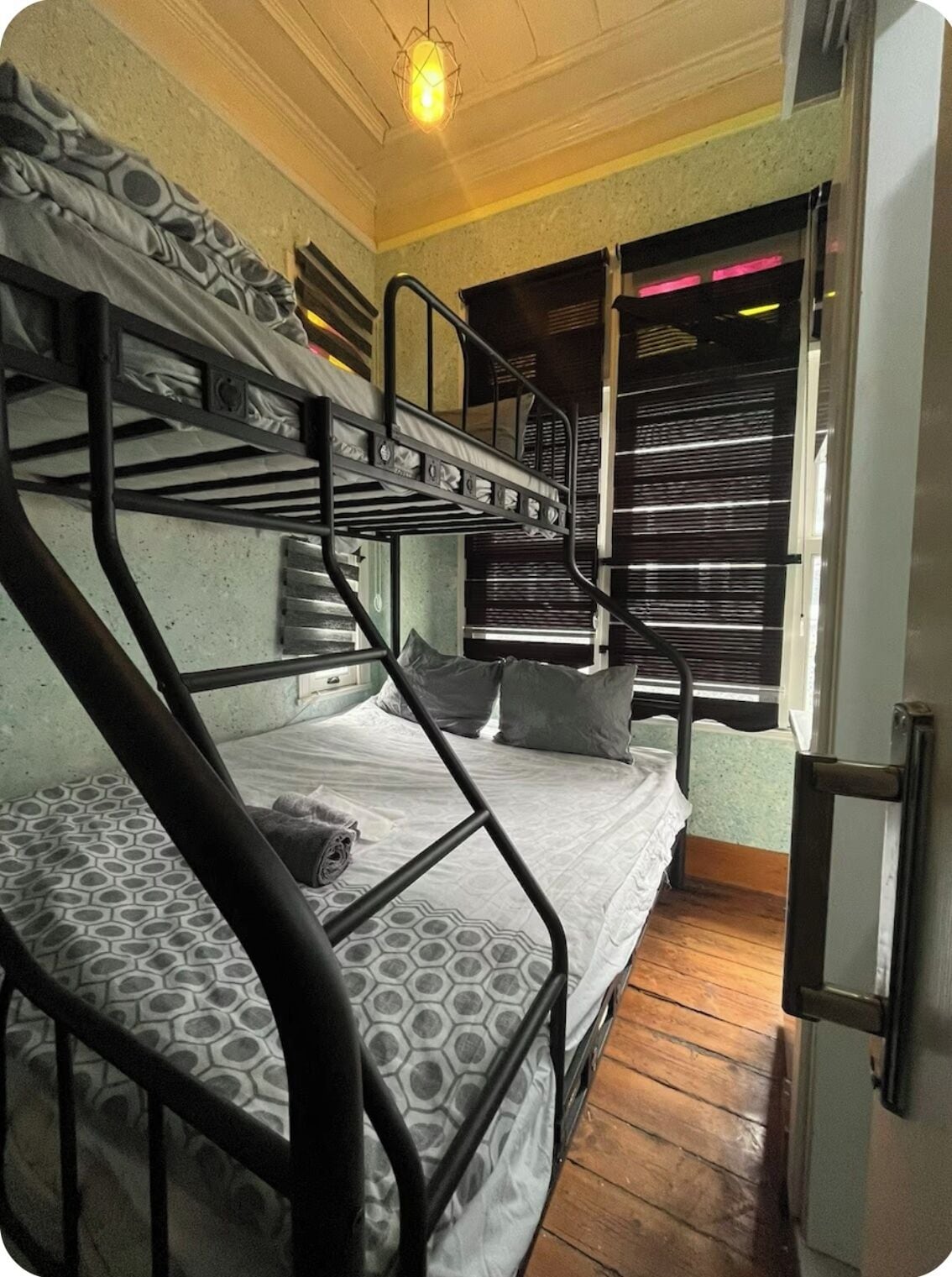 Habitación con literas, colchón estampado, lámpara colgante y ventana con persianas.