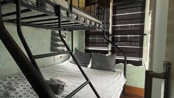 Habitación con literas, colchón estampado, lámpara colgante y ventana con persianas.