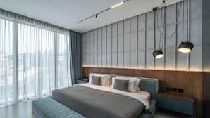 Un dormitorio moderno con una cama grande, un banco, una mesita de noche y un aplique de pared.